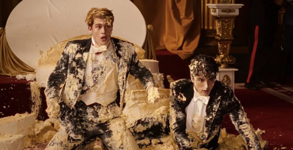 nicholas galtizine and taylor perez covered in cake wearing suits in article about red white & royal blue book differences