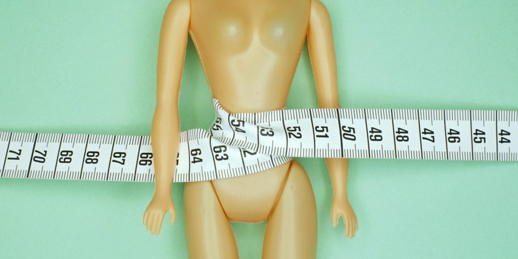 Female doll with tape measure around waist, portrait