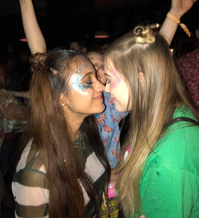Two girls smiling at each other, with their eyes closed, wearing festival style clothing and glitter