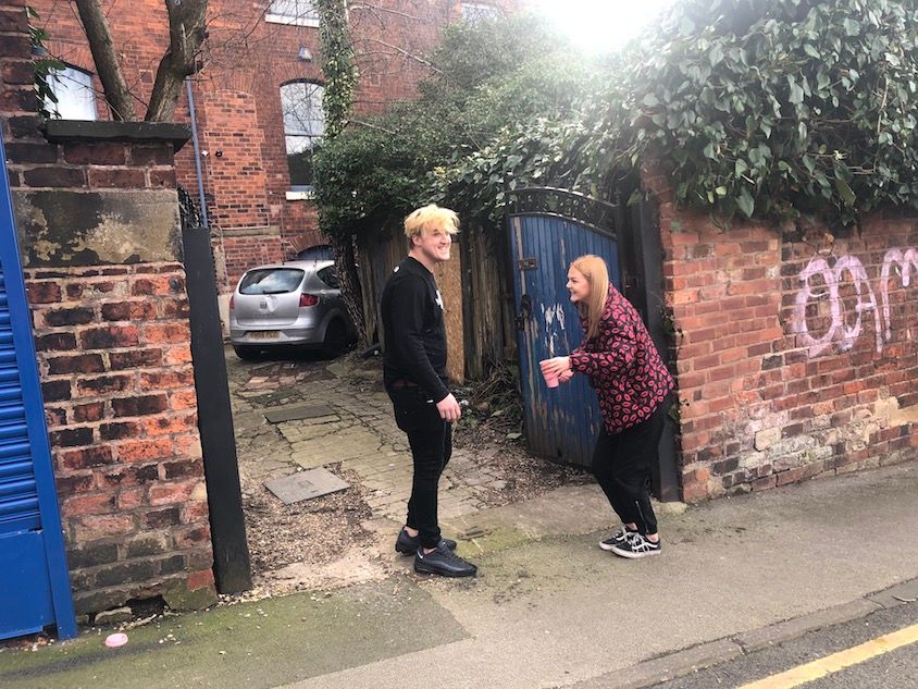 Image may contain: Street, Town, Building, City, Urban, Wall, Tarmac, Asphalt, Jacket, Blazer, Road, Plant, Vegetation, Coat, Overcoat, Shoe, Footwear, Brick, Car, Transportation, Automobile, Vehicle, Apparel, Clothing, Person, Human