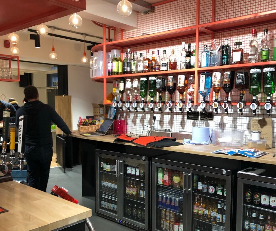 Image may contain: Bottle, Plywood, Bar Counter, Beverage, Drink, Alcohol, Wood, Shelf, Pub, Person, Human