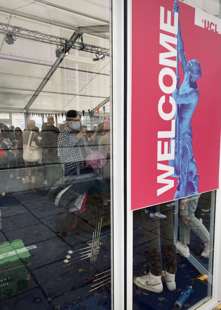 Photo taken from outside a glass wall showing a crowd inside a room with a pink and blue 