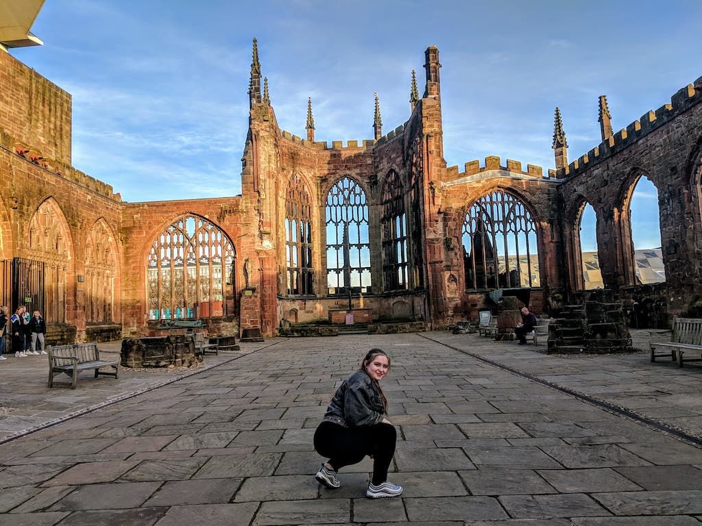 Image may contain: Cathedral, Church, Tower, Spire, Steeple, Downtown, Urban, City, Town, Furniture, Bench, Apparel, Shoe, Clothing, Footwear, Path, Walkway, Building, Architecture, Flagstone, Person, Human