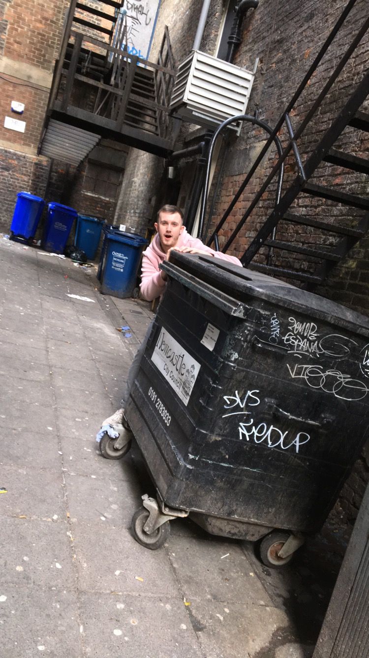 Image may contain: Trash Can, Can, Path, Wood, Alley, Alleyway, Clothing, Apparel, Pants, Tin, Flagstone, Brick, Urban, Building, Street, Road, Town, City, Human, Person