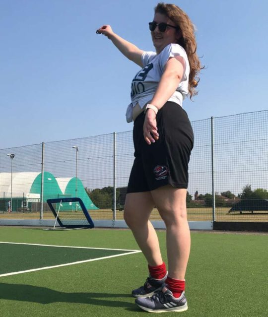 Lara posing with right arm up on a hockey astroturf in the sunshine