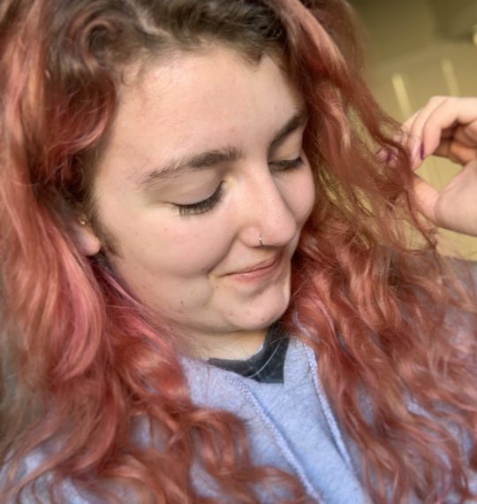 Lara smiling looking down with pink hair