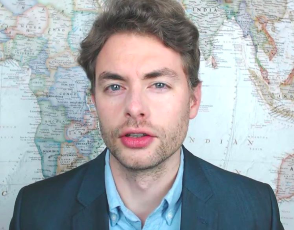 Paul Joseph Watson appears in front of a world map, the picture is a still during a to camera piece by the Infowars presenter and now Editor-at-Large