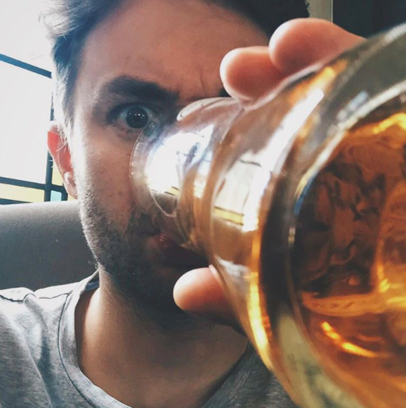 A close up shot showing Paul Joseph Watson drinking a pint of beer, his eyes are wide and his brow furrowed