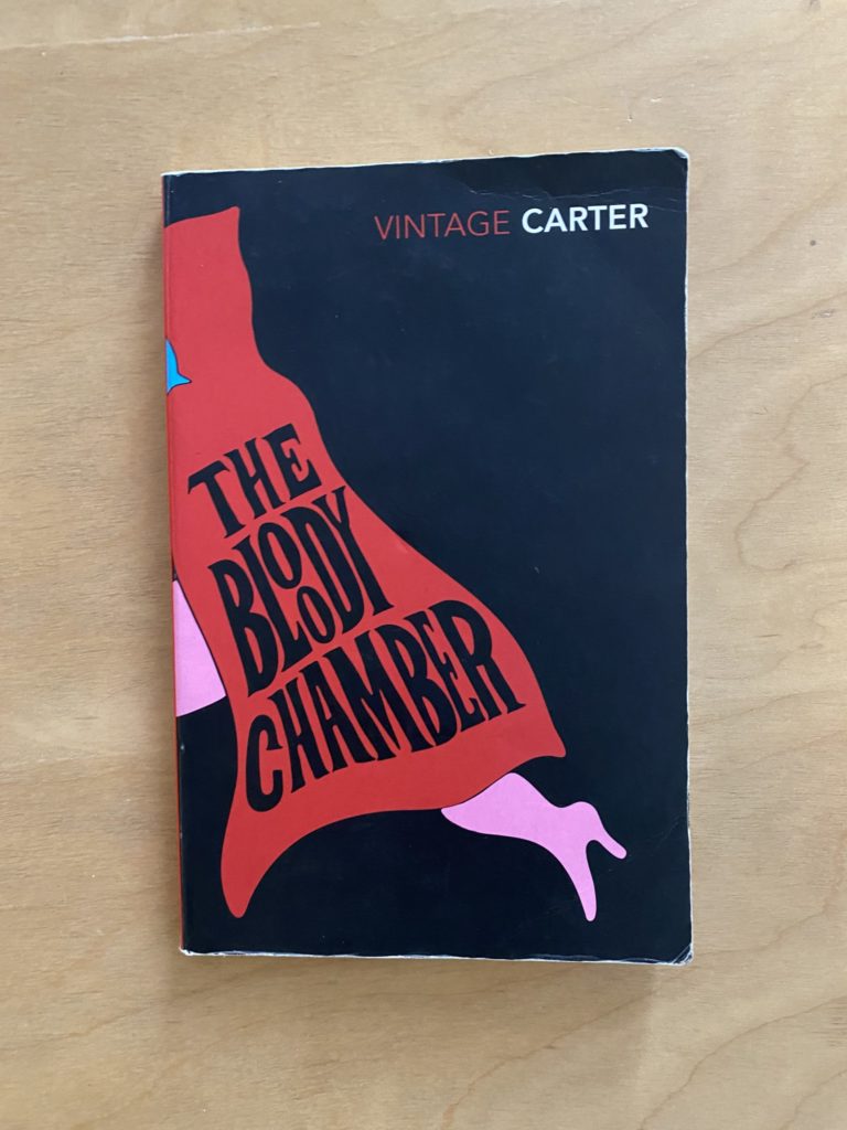 A black book with a woman in a red cape running on it. the title of the book is in black on the cape.