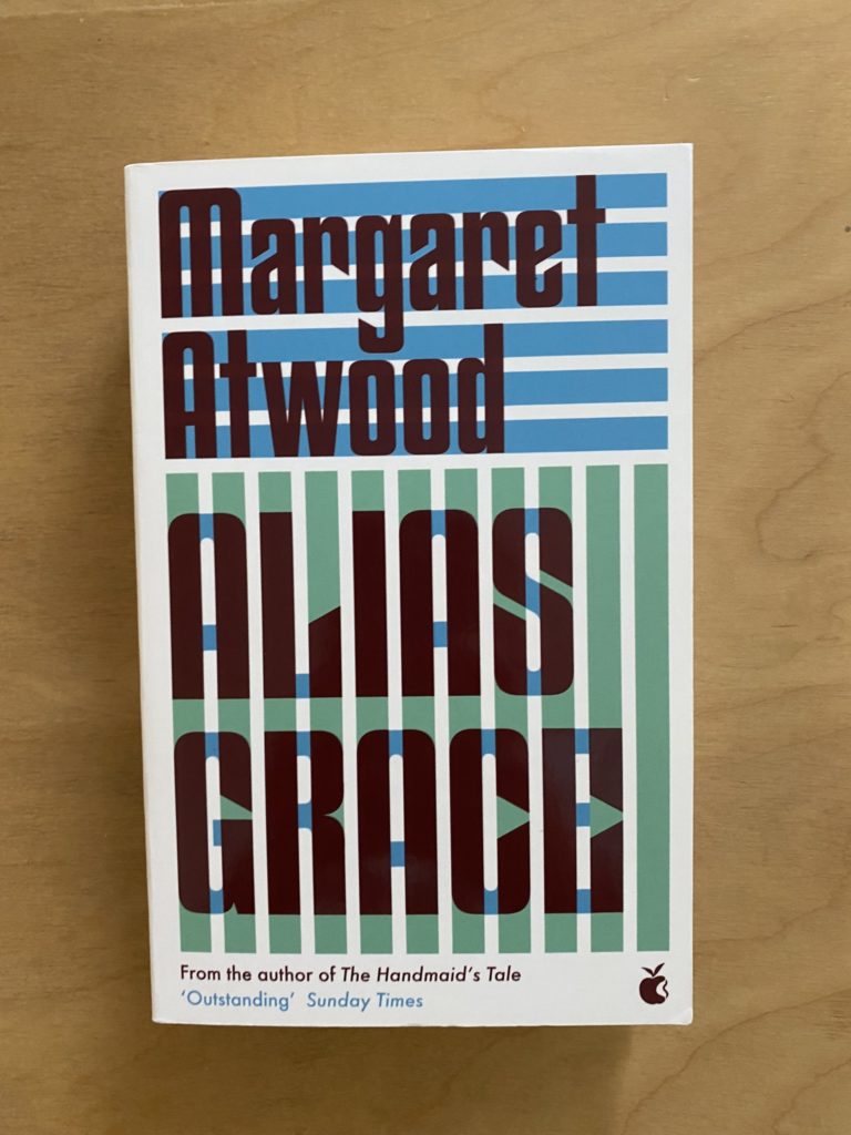 A white book with a blue and green geometric patten on with title of the book and author's name in brown.