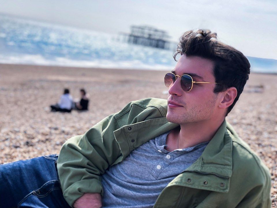 Image may contain: Man, Face, Sleeve, Jacket, Coat, Apparel, Clothing, Beach, Coast, Shoreline, Human, Person, Outdoors, Sea, Ocean, Water, Nature, Accessories, Accessory, Sunglasses