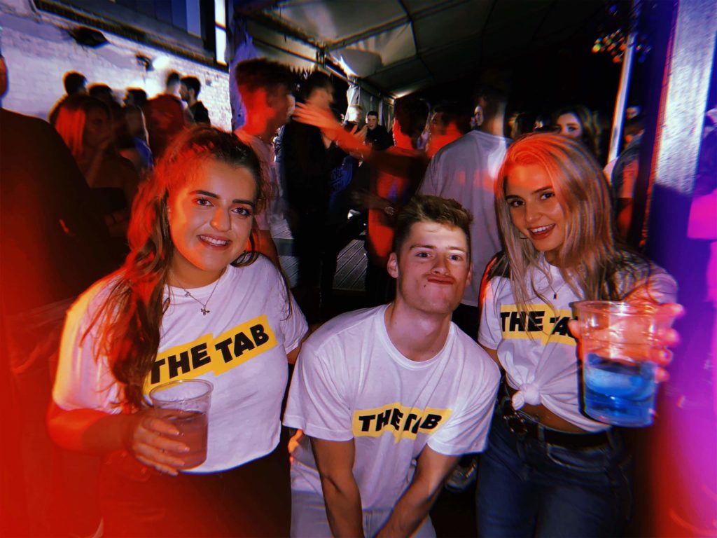 3 students in Tab t-shirts holding drinks and smiling
