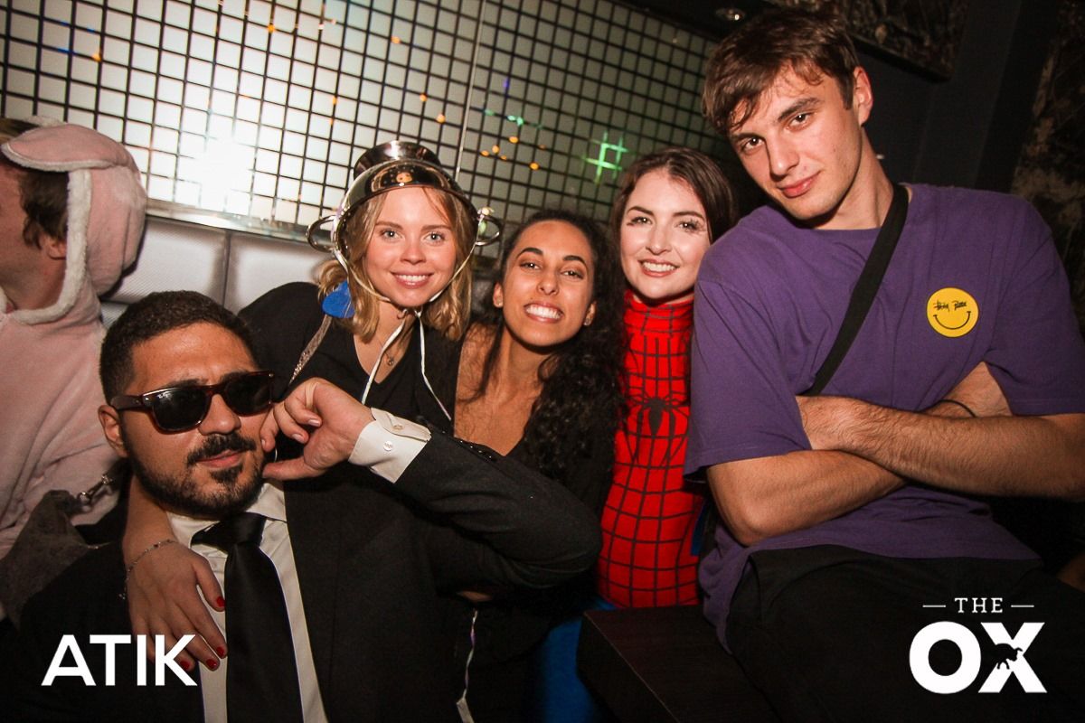 Image may contain: Night Club, Suit, Coat, Overcoat, Bar Counter, Pub, Club, Hat, Apparel, Clothing, Sunglasses, Accessory, Accessories, Tie, Human, Person