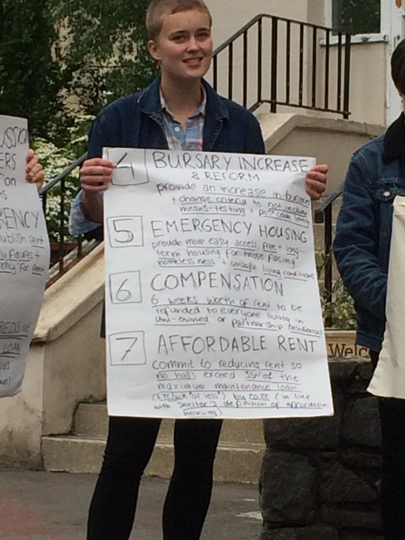 Image may contain: Banner, Handwriting, Apparel, Clothing, Crowd, Human, Person, Text