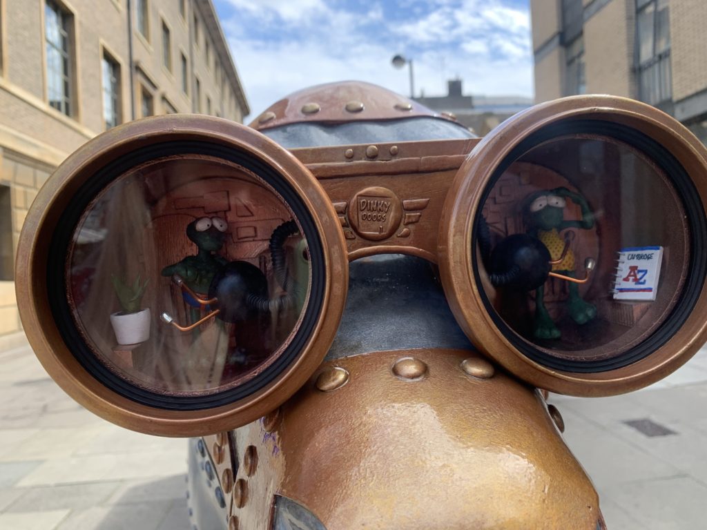 Close up of a mechanical cow depicting two small aliens in the goggles