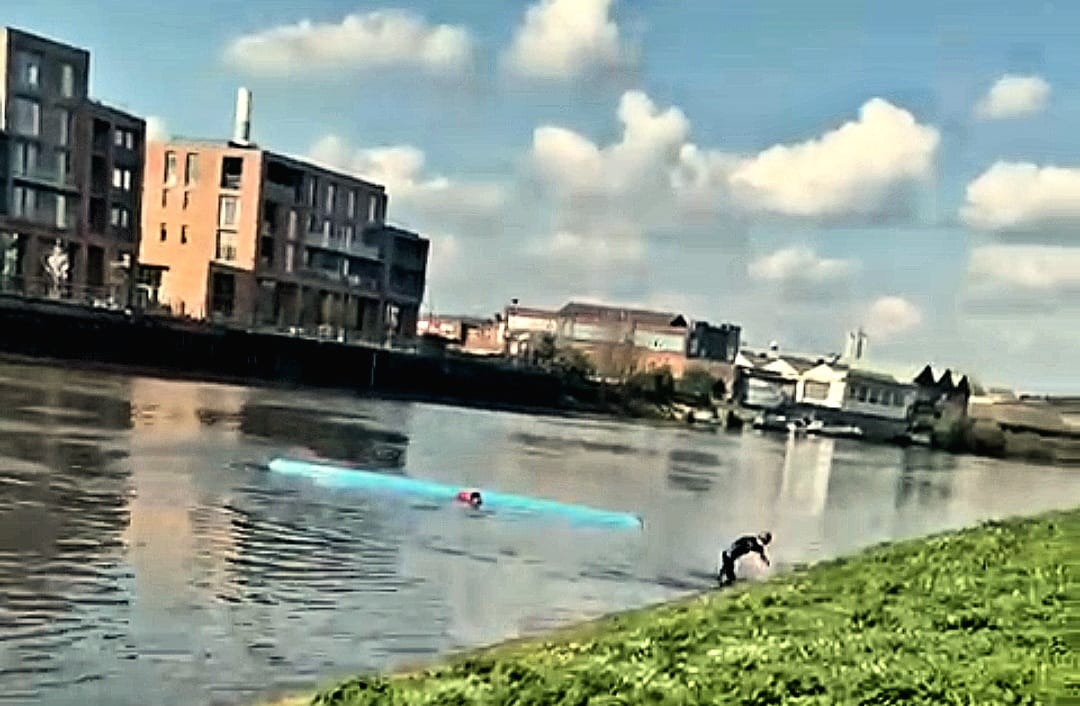 A person holding onto a capsized boat while another is swimming away from it.