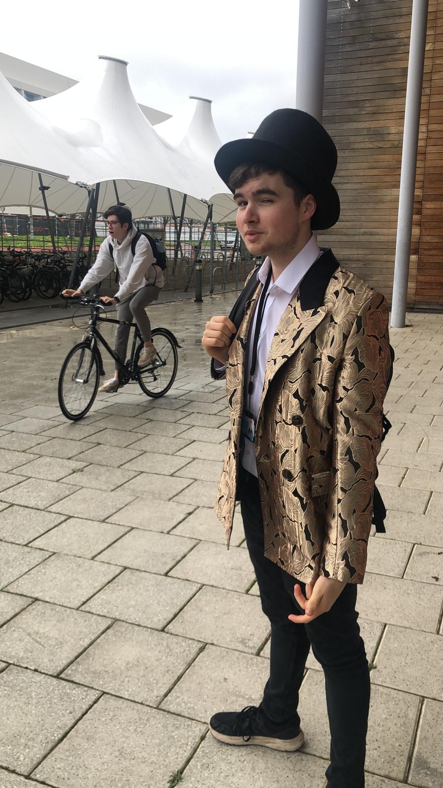 A person wearing a gold blazer and top hat