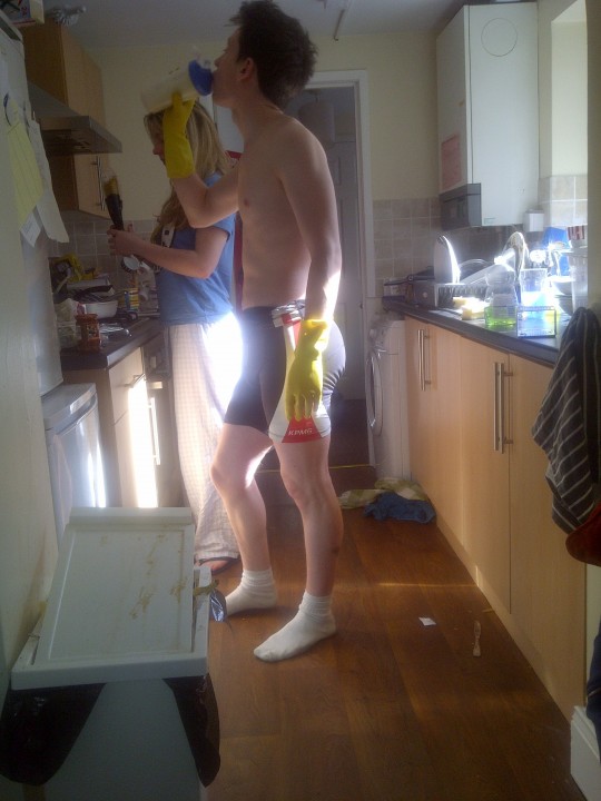 A rower trying to clean the kitchen whilst drinking a protein shake