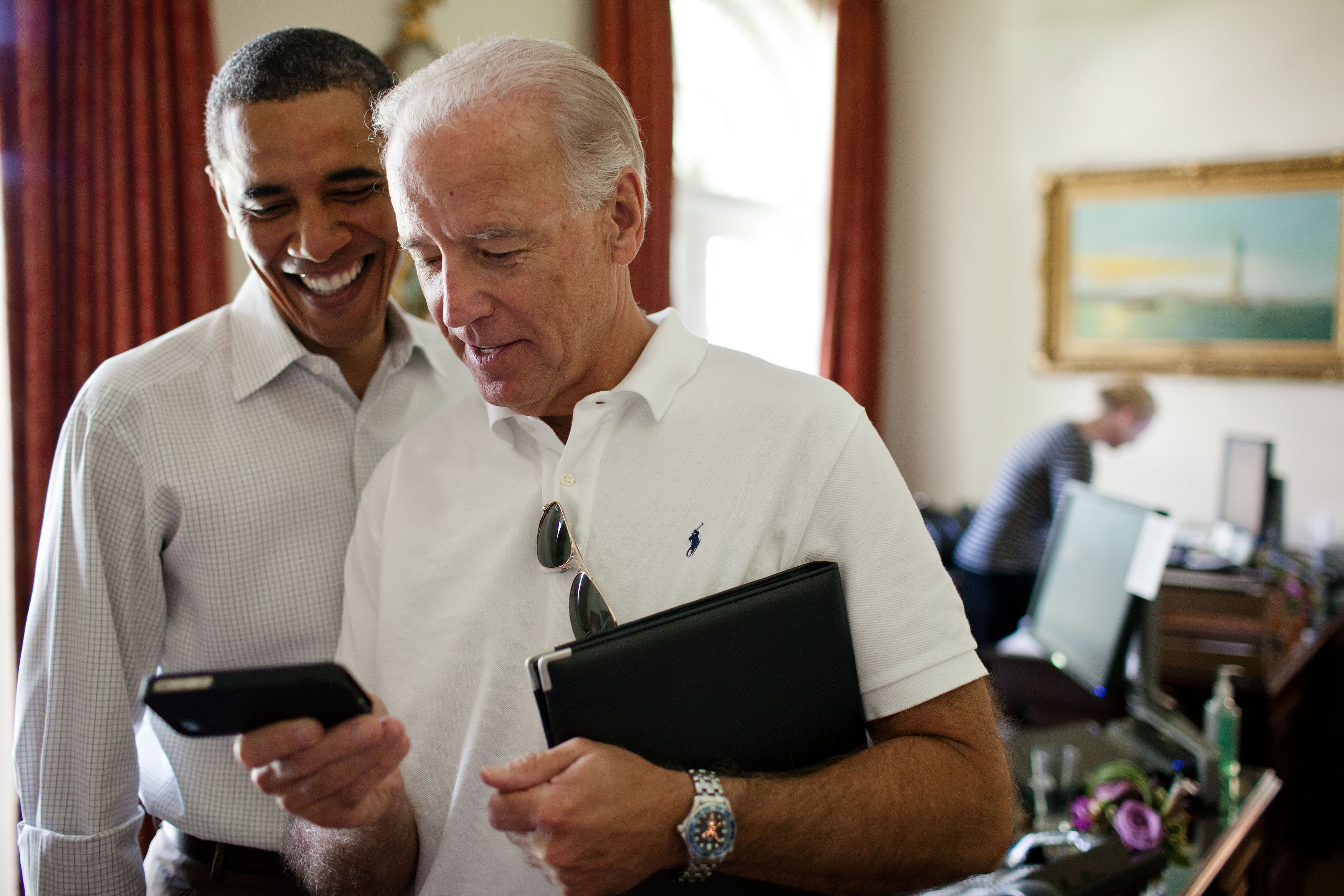 Vice President Joe Biden and President Barack Obama look at an app on an iPhone in the Outer Oval Office, Saturday, July 16, 2011. (Official White House Photo by Pete Souza) This official White House photograph is being made available only for publication by news organizations and/or for personal use printing by the subject(s) of the photograph. The photograph may not be manipulated in any way and may not be used in commercial or political materials, advertisements, emails, products, promotions that in any way suggests approval or endorsement of the President, the First Family, or the White House.