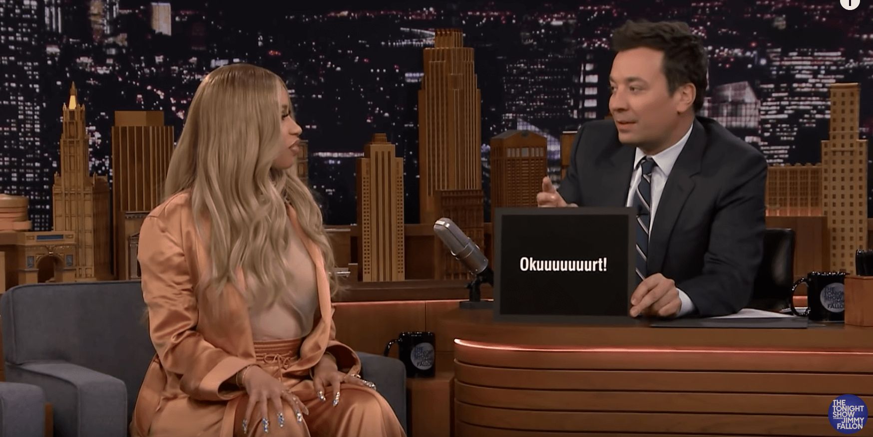 Image may contain: Okurrr, Cardi B, trademark, Jimmy Fallon, meaning, origin, Okurr, Tie, Accessories, Accessory, Crowd, Apparel, Clothing, Suit, Coat, Overcoat, Human, Person