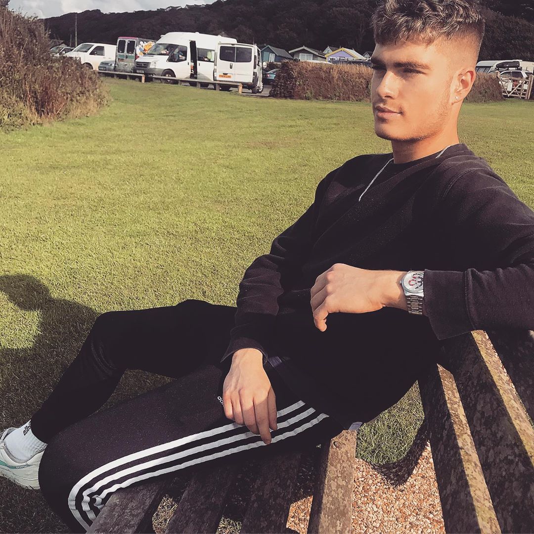 Image may contain: Great British Bake Off 2019, Jamie Finn, Jamie, cast, contestants, lineup, Instagram, age, GBBO, Bake Off, 2019, start date, Channel 4, Bench, Footwear, Furniture, Sitting, Human, Person, Plant, Grass, Apparel, Clothing