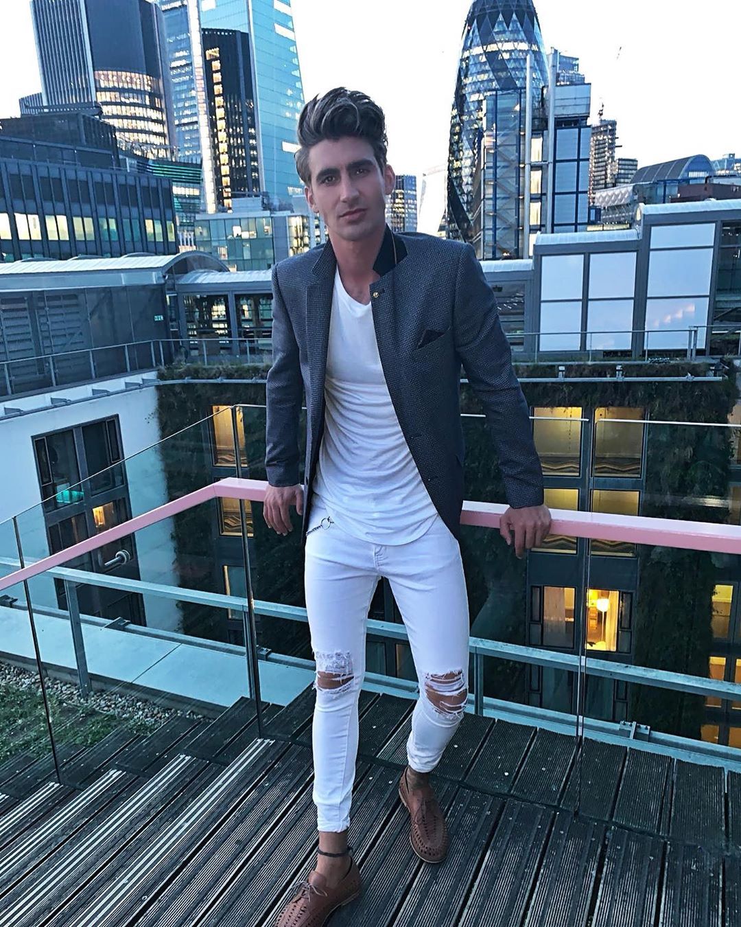 Image may contain:  Love Island 2019 contestants, Love Island, 2019, now, job, Instagram, updates, news, latest, series five, Chris Taylor, High Rise, Suit, Overcoat, Metropolis, Town, City, Urban, Building, Person, Human, Coat, Blazer, Jacket, Apparel, Clothing
