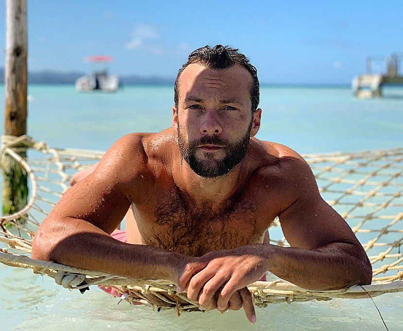 Image may contain: The I-Land cast, The I-Land, island, Netflix, Kyle Schmid, Moses, stars, films, tv, series, Instagram, age, job, Man, Apparel, Clothing, Undershirt, Person, Human, Furniture