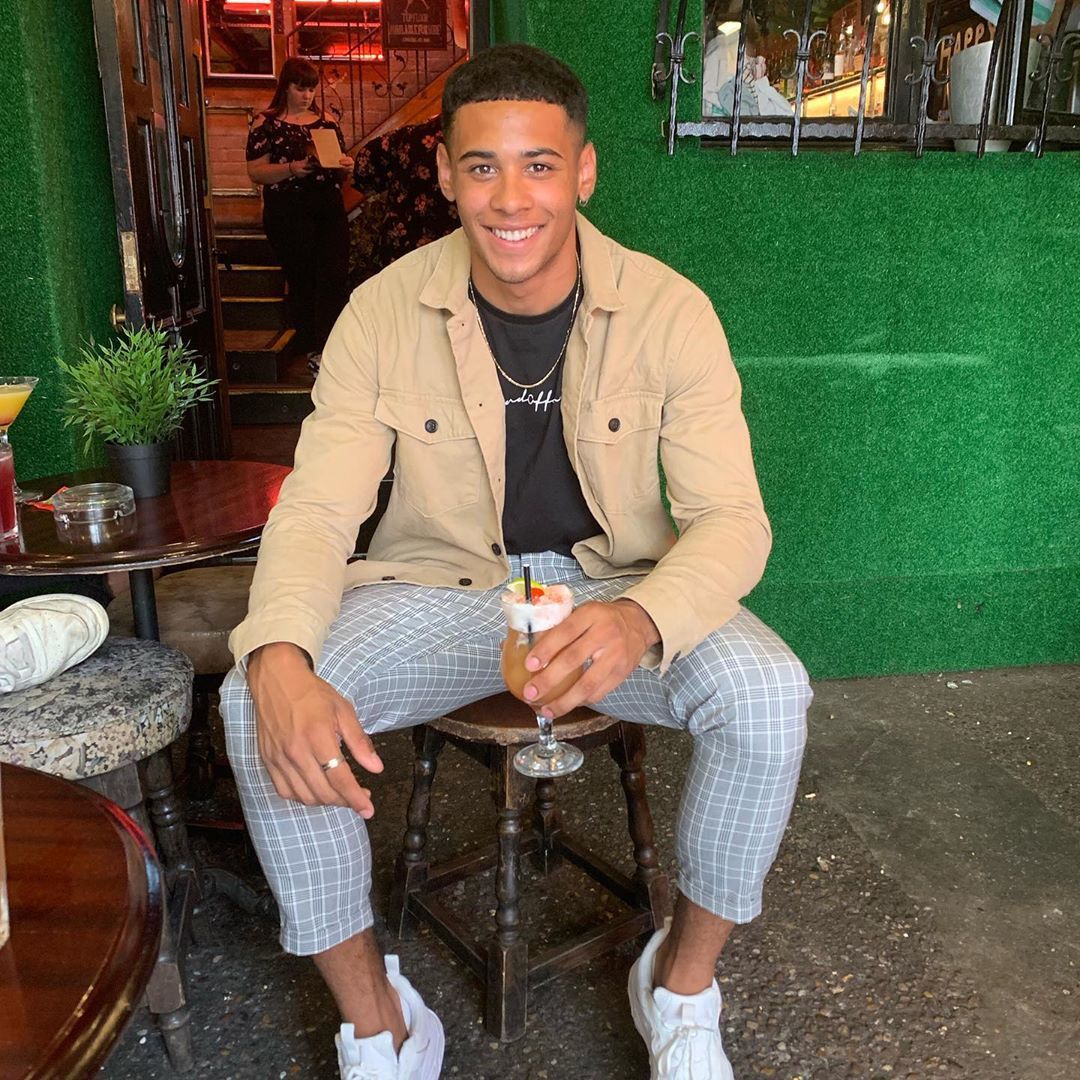 Image may contain: first winter Love Island contestant, winter, Love Island, Ellis Iyayi, 2020, cape town, south africa, contestant, cast, lineup, rumours, fitness, instructor, man, boy, new, Pub, Bar Counter, Pants, Long Sleeve, Sleeve, Restaurant, Plywood, Wood, Sitting, Shoe, Footwear, Human, Person, Clothing, Apparel