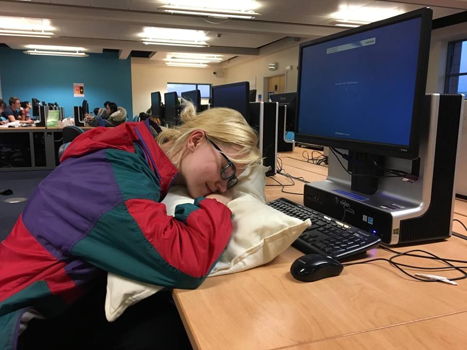 a student pretending to sleep at a desk at a library at cardiff university
