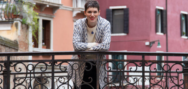 Woman (Kim Sherwood) leaning on a bridge with a Venetian building behind her
