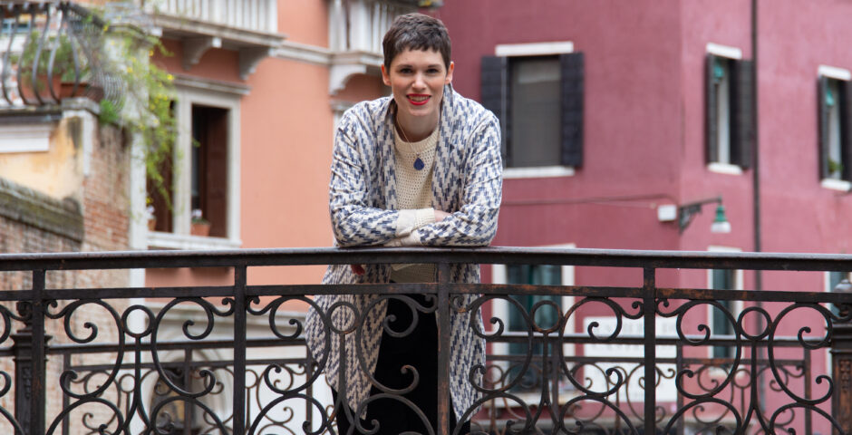 Woman (Kim Sherwood) leaning on a bridge with a Venetian building behind her